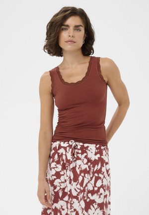 Mujer con cabello corto y castaño, vistiendo una blusa sin mangas de color óxido con ribete de encaje y pantalones de talle alto con estampado floral y cordón ajustable.
