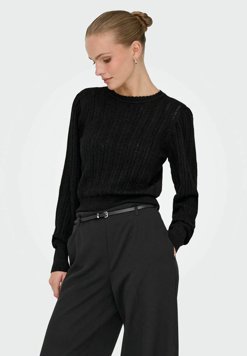 Pull en tricot côtelé noir à manches longues et col festonné, associé à un pantalon noir taille haute et une fine ceinture noire.