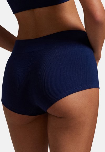 Pantaloncini in cotone blu navy a costine con una fascia larga in vita. Presentano una texture liscia e un design aderente, che mette in risalto la curvatura della figura.