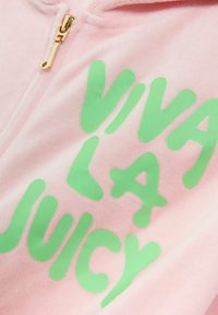 Ružová mikina na zips vyrobená z jemného materiálu, s odvážnym zeleným textom "VIVA LA JUICY" s lesklým povrchom a zlatým zipsom.