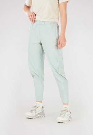 Light green athletic pants with elastic waist, tapered fit, side pockets, and subtle logo detail, paired with white sneakers and crew socks.