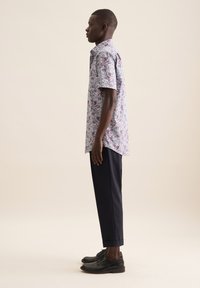 Camicia a maniche corte con un motivo floreale viola; abbinata a pantaloni neri a sigaretta e scarpe nere con lacci. Design minimalista.