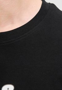 Sort bomulds t-shirt med rund halsudskæring. Har en glat tekstur og diskret syning langs kraven, hvilket fremhæver et minimalistisk design.