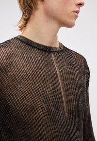 Top preto transparente de manga comprida com nervuras verticais, decote redondo e brilho subtil; apresenta uma fenda frontal para adicionar textura.