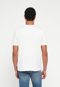 Λευκό βαμβακερό μπλουζάκι με στρογγυλή λαιμόκοψη, κοντά μανίκια και ίσια γραμμή, φορεμένο από έναν άνθρωπο που είναι γυρισμένος από την πλάτη, σε συνδυασμό με μπλε τζιν.