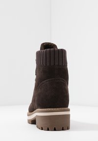 Brązowy zamszowy botek za kostkę z ryflowanym kołnierzem, słupkiem i teksturowaną podeszwą dla lepszej przyczepności. Posiada detale przeszycia po bokach.