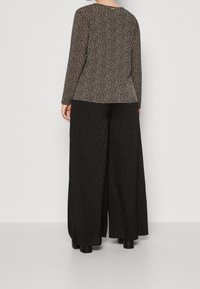 Maglietta a maniche lunghe con un motivo leopardato nero e beige, abbinata a pantaloni neri a gamba larga con dettagli testurizzati. Calzature nere completano il look.