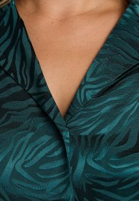 Tissu à motif zèbre en teal foncé et noir, comportant un col châle et une surface finement texturée avec un léger éclat.