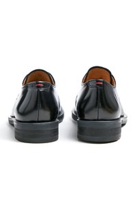 Schwarze Lederschuhe mit einer glatten, glänzenden Oberfläche. Rund geschnittene Zehenform, niedriger Absatz, sichtbare Nähte und dezente rote Akzente an der Rückseite.