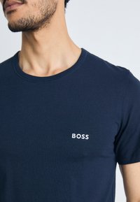 T-shirt de algodão azul marinho com decote redondo e mangas curtas. Apresenta um logótipo branco bordado "BOSS" no lado esquerdo do peito.