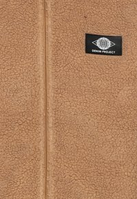 Vaaleanruskea fleece-takki, jossa on teksturoitu pinta. Takissa on keskellä vetoketju ja musta PÄÄLLYS nimeltä "DENIM PROJECT". Yksinkertainen, käytännöllinen muotoilu.