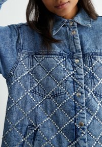 Denim jacket featuring a light blue color with a quilted diamond pattern, accented by silver studs and metal snap buttons.