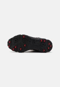 Suela de zapato negra con surcos profundos y agarraderas triangulares rojas, mostrando el nombre de la marca "POLO" grabado en el centro sobre un fondo blanco.
