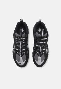 Des chaussures de sport noires et grises avec une surface texturée, des lacets ronds, des accents réfléchissants et un logo swoosh prominent sur le bout.