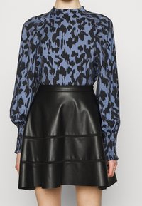 Bluse med blomsterprint i blå med sorte detaljer, udformet med pufærmer; parret med en sort faux læder A-line nederdel med lagdelt tekstur.