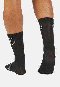 Black socks with a ribbed texture and a solid design. Features white printed accents on the side and a reinforced heel.