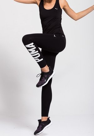 Top sportivo senza maniche nero e leggings con il logo Puma in bianco. Scarpe da ginnastica con motivo nero e viola.