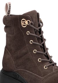 Botină din suede maro, cu vârf rotund, accente din metal auriu, șireturi tonale și un exterior texturat. Dispune de o talpă din cauciuc negru.
