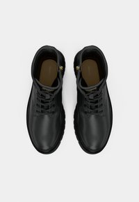 Para czarnych skórzanych botków za kostkę z sznurówkami, z solidnymi podeszwami, widocznych z góry na białym tle.