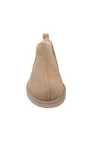 Bottine en suede beige avec un bout arrondi, doublure douce et un petit tab au dos pour un enfilage facile. Design minimaliste avec des détails de couture.