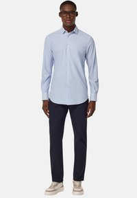 Camicia a righe azzurro chiaro con colletto botton down, maniche lunghe e bottoni bianchi, abbinata a pantaloni blu scuro e sneakers neutre.