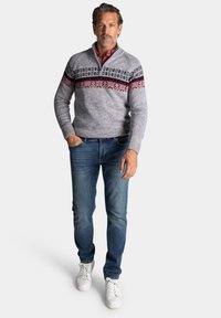 Grijze gebreide trui met een kwart rits, met een gestreept ontwerp in rood en marineblauw over de borst. Gecombineerd met blauwe jeans en witte sneakers.