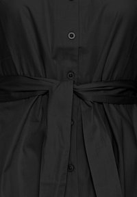 Abito nero con chiusura a bottoni frontale, cintura in vita e una texture leggera e liscia. Il tessuto ha una leggera lucentezza e un design fluido.