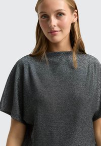 Čierny kovový top s krátkym rukávom, vo voľnom strihu a s vysokým golierom, s lesklou textúrou a mäkkou tkaninou.