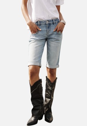 Shorts en denim bleu clair avec des ourlets retournés, associés à des bottes en cuir noir montant jusqu'aux genoux avec des accents en clous argentés.