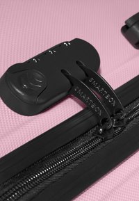 Lucchetto combinato nero che fissa due cursori delle cerniere su una superficie rosa testurizzata di una valigia.