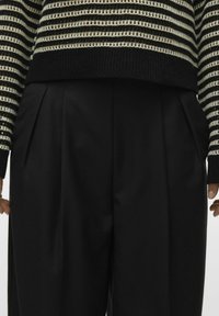 Pantalons larges noirs avec plis sur le devant, associés à un pull rayé noir et crème. Le pull présente un ourlet et des poignets côtelés.