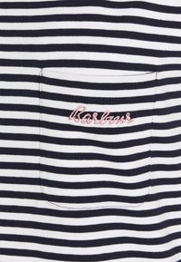 Niebiesko-biały materiał w paski z małą kieszonką z różowym haftowanym napisem "Barbour".