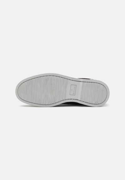 Svart sneaker med texturerad gummisula. Yttersulan har vågmönster och en rektangulär logotypetikett nära hälen.