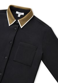 Zwarte button-up shirt met borstzak en bruine kraag met witte rand, plat weergegeven op een witte achtergrond.