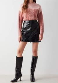 Pink and cream cable-knit sweater paired with a black faux leather mini skirt featuring a front zipper. Black knee-high heeled boots complete the look.