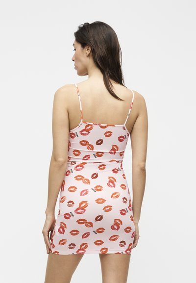 Γυναίκα με πλάτη, φοράει ένα ροζ φόρεμα με σχέδιο κόκκινων και πορτοκαλί χειλιών και λεπτές τιράντες.