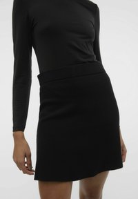 Jupe mini noire en tissu texturé, dotée d'une taille large et d'un ourlet légèrement arrondi. Portée avec un haut ajusté à manches longues.