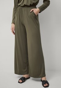 Olijfgroene wijde broek, gemaakt van soepele stof, met een elastische tailleband en zijzakken. Gekocht met zwarte instapsandalen.