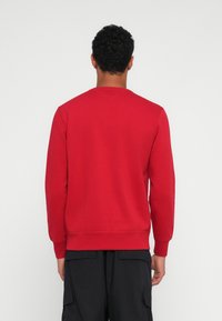 Felpa rossa a collo rotondo realizzata in cotone. Presenta polsini e bordo a coste, una trama liscia e un design semplice, privo di decorazioni.