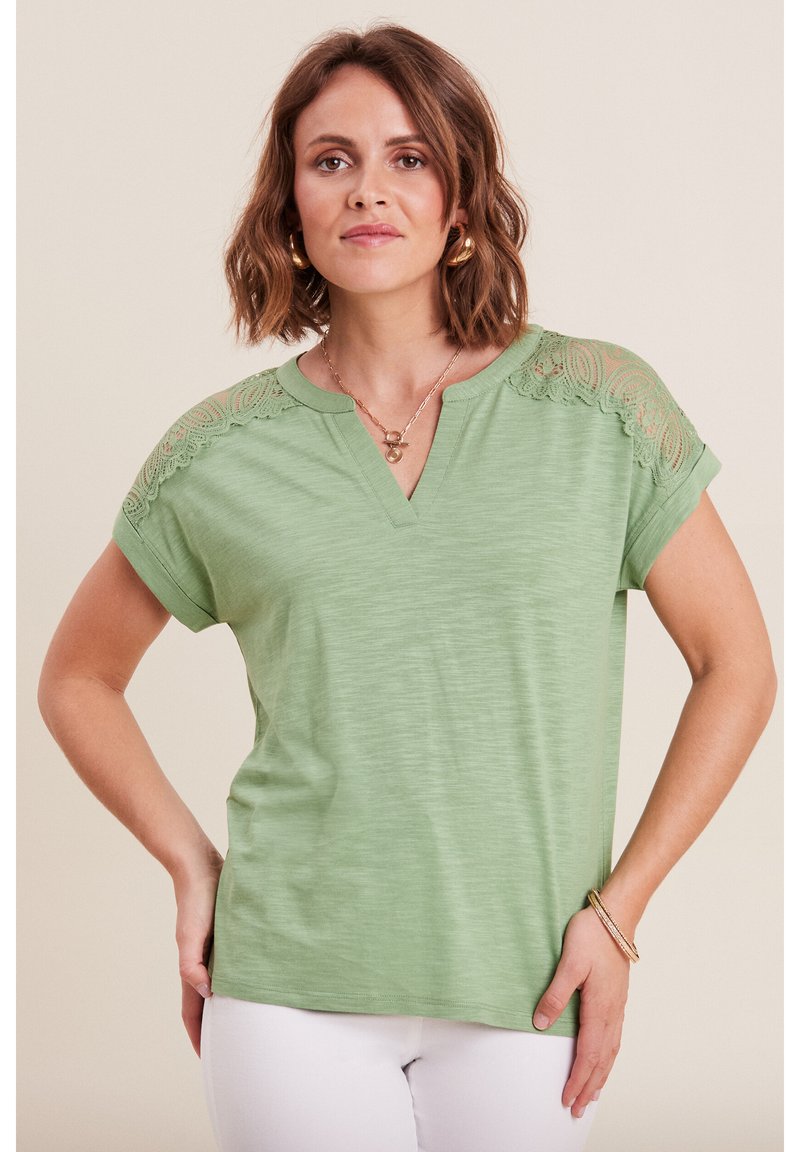 Helles grünes V-Ausschnitt-T-Shirt mit kurzen Ärmeln, das auf den Schultern mit filigranen Spitzelementen verziert ist und einen lockeren Schnitt hat. Glatte Textur.