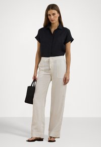 Melnas īsām piedurknēm krekls ar pogām, brīvi beigu linu bikses ar gumijotu jostu, un austs melns rokas soma. Izskatu papildina vienkārši zābaki.