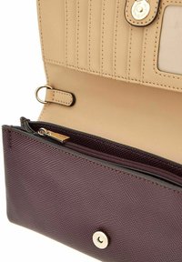 Portefeuille texturé violet avec une doublure beige, doté de plusieurs emplacements pour cartes, d'une poche zippée et d'une fermeture à bouton-pression.