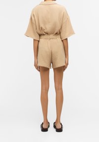 Ensemble deux pièces beige clair avec un haut à col, ample, et un short assorti à taille élastique, présentant un tissu texturé.