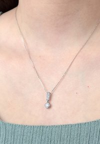 Collier en argent avec un pendentif en forme circulaire orné d'une pierre transparente, suspendu à une chaîne texturée décorée de petites pierres précieuses rectangulaires.