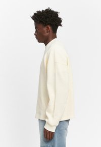 Creme lange mouwen waffle-knit sweatshirt met een ontspannen pasvorm, geribde manchetten en een ronde hals, gecombineerd met lichtblauwe denim jeans.