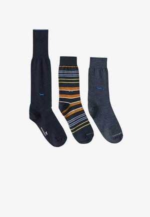 Tre par sokker: venstre er ensfarvet mørkeblå, centrum har et stribet mønster i blå, orange og gul, højre er ensfarvet mørkegrå.