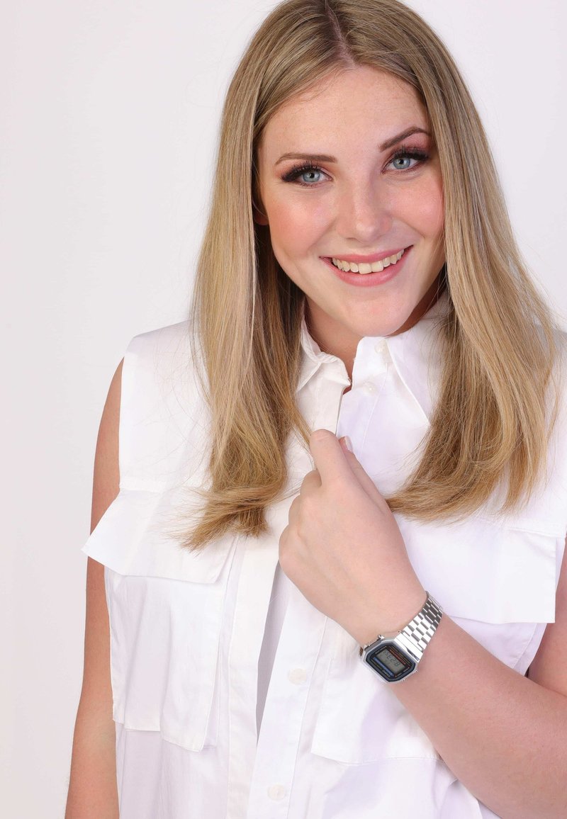 Chemisier sans manches blanc avec des détails froncés, texture lisse, et montre argentée avec un cadran rectangulaire et un bracelet métallique, portée au poignet.
