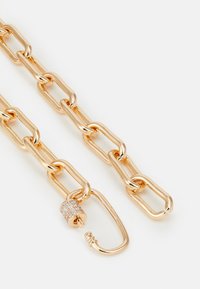 Goldfarbene Kette aus ineinandergreifenden Gliedern mit einer glänzenden, strukturierten Oberfläche. Enthält einen Verschluss, der mit kleinen klaren Strasssteinen verziert ist.