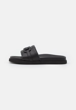 Black slide sandals made of smooth leather, featuring a wide strap with a decorative buckle. Flat rubber sole with textured grip.