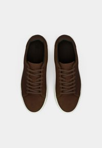 Sneaker in pelle marrone con punte arrotondate, lacci piatti e superficie testurizzata. Suole in gomma bianca. Design semplice senza marchi visibili.